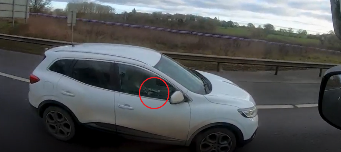 Caption: Footage of this car driver holding her mobile phone up to talk into as she drives one-handed along the M40 can be seen here